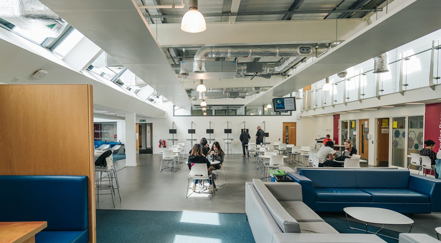 An open university study space with students gathered around tables, engaged in study and conversation.